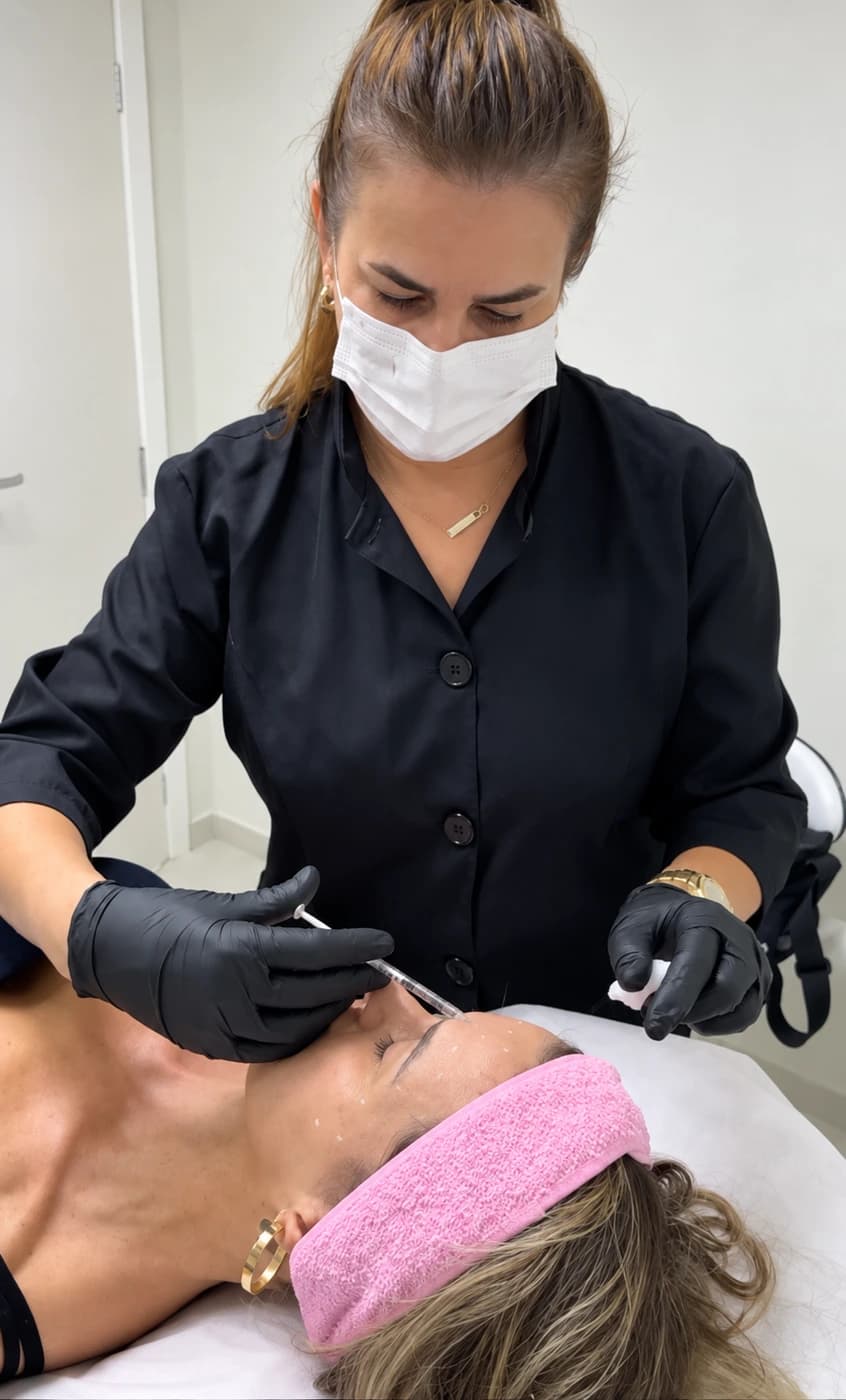 Adenilda de máscara e luvas durante um atendimento facial